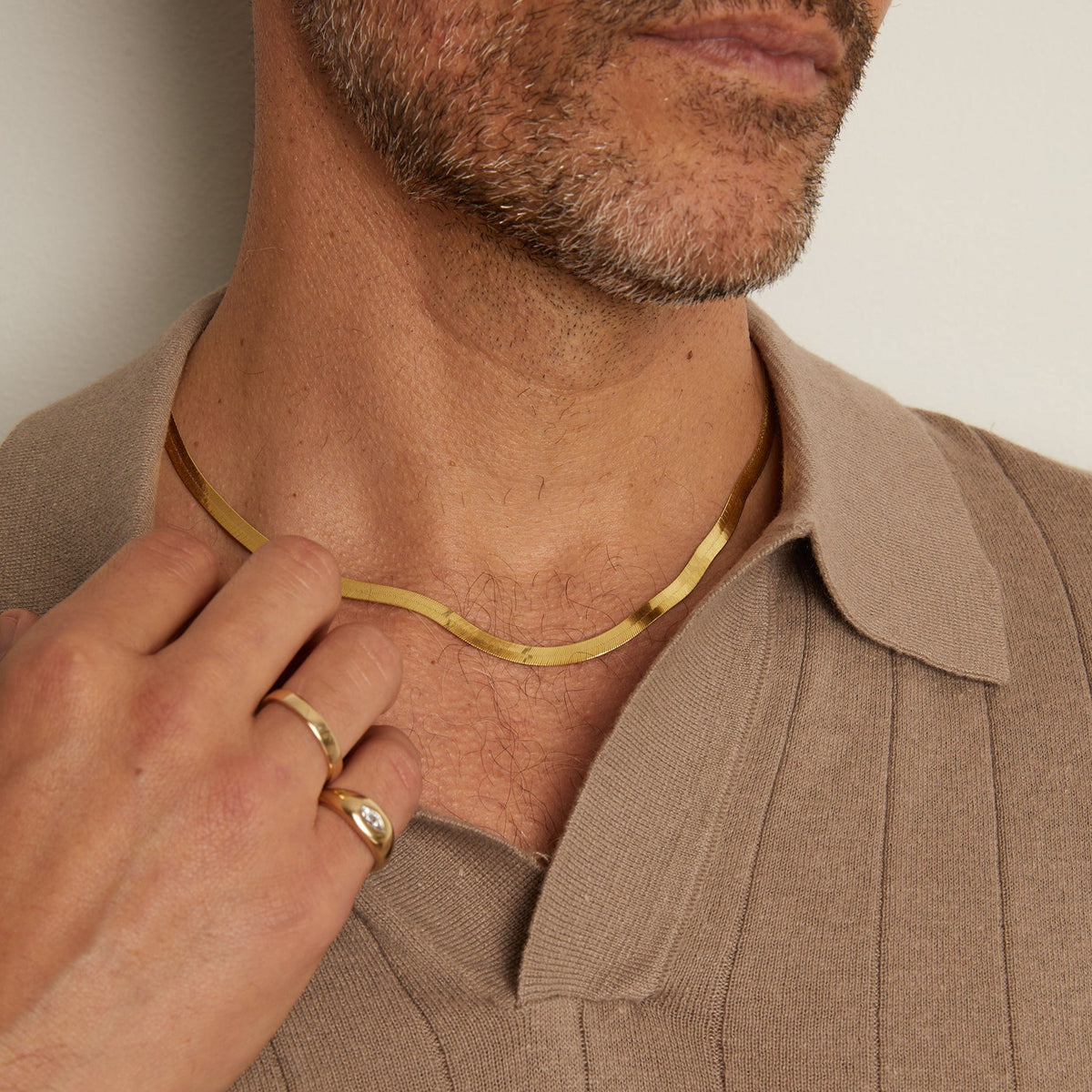 Model. Man wearing a gold necklace and ring, with a neutral background
