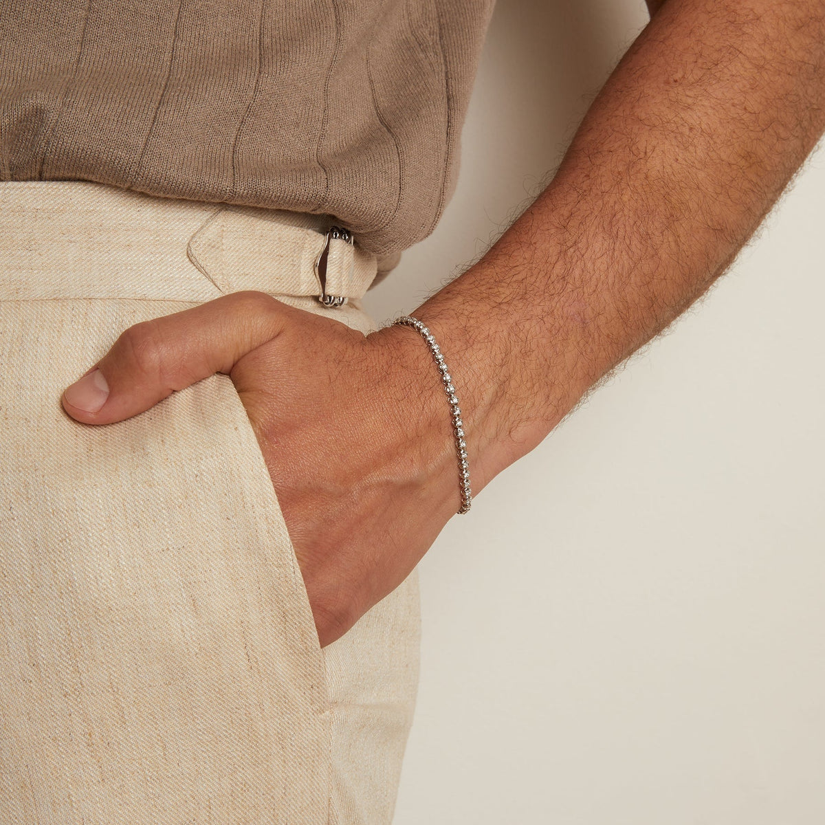 Model. Person wearing a beige shirt and pants with a bracelet on a neutral background
