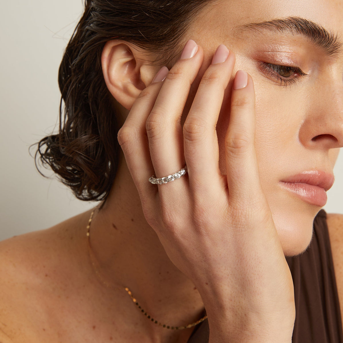 Model. Close-up of a woman's hand with a ring on her finger, touching her face.