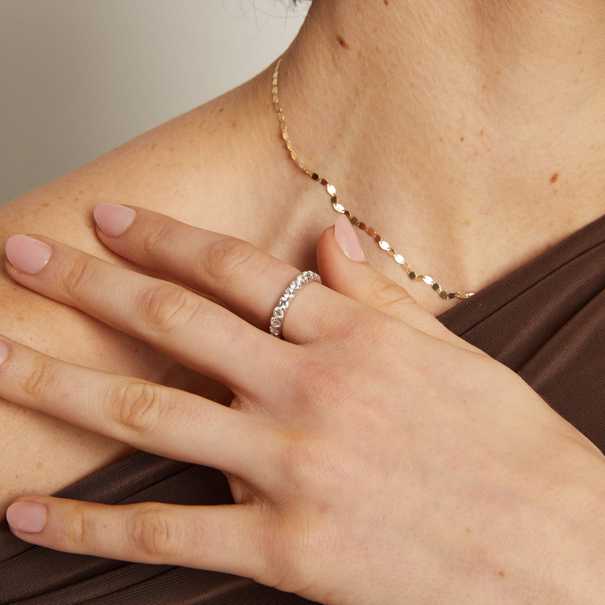 Model. Close-up of a person wearing a gold necklace and ring on a neutral background