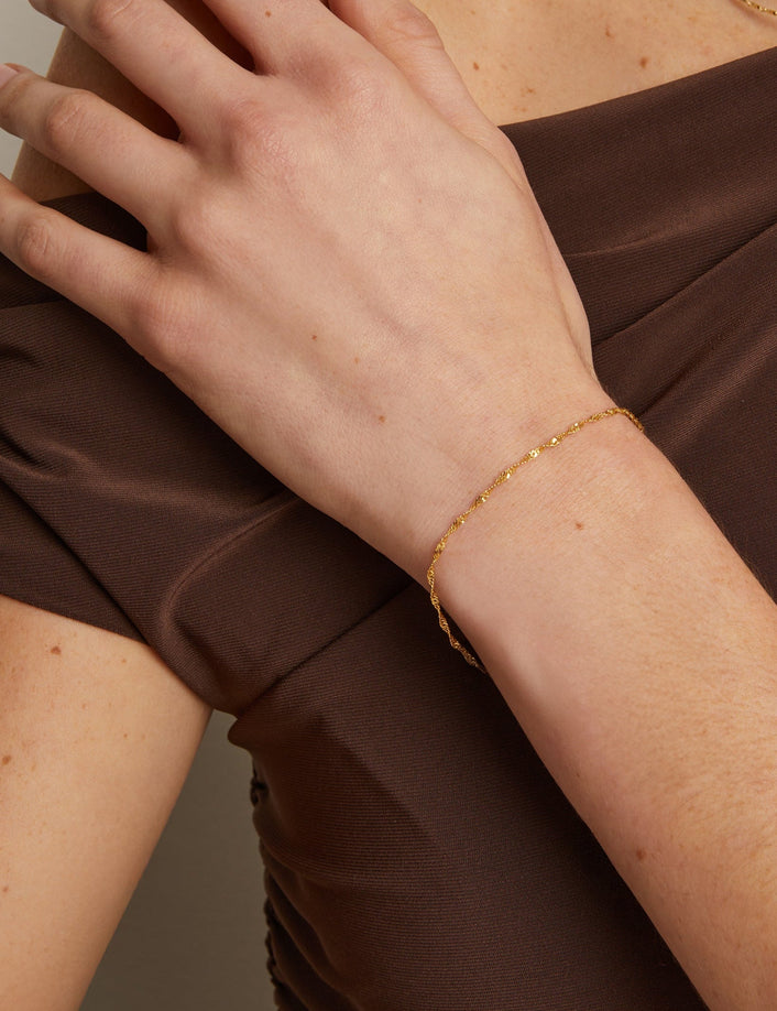 Model. Person wearing a brown dress with a gold bracelet and necklace against a neutral background