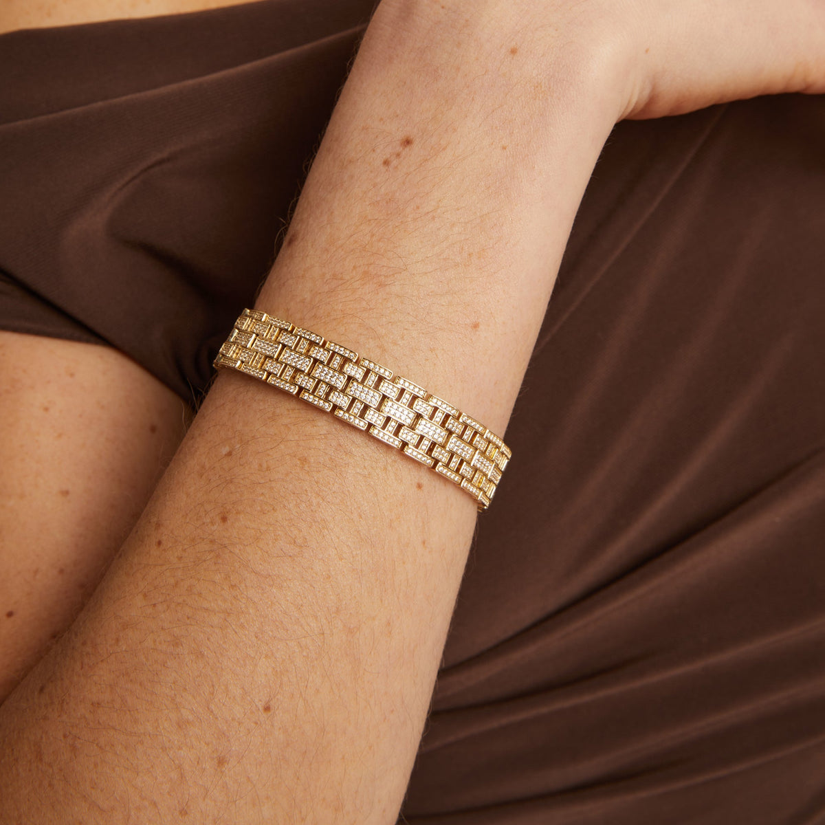 Model. Gold bracelet on a person's wrist with a brown fabric background