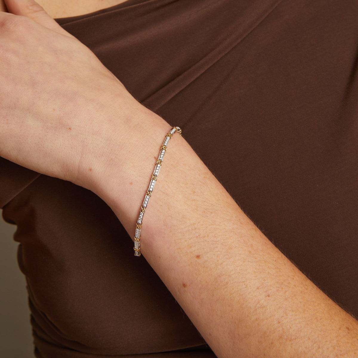 Close-up of a person's arm wearing a diamond bracelet against a brown background