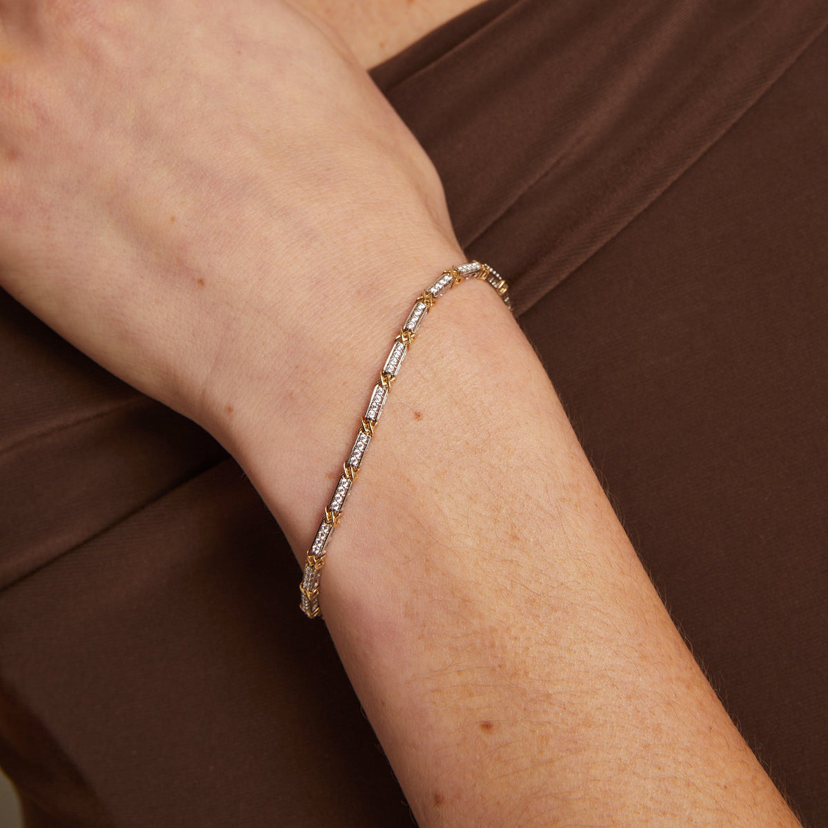 Model. Close-up of a person wearing a gold bracelet on a neutral background