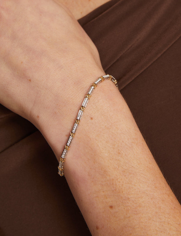 Gold bracelet with clear stones on a wrist against a brown background