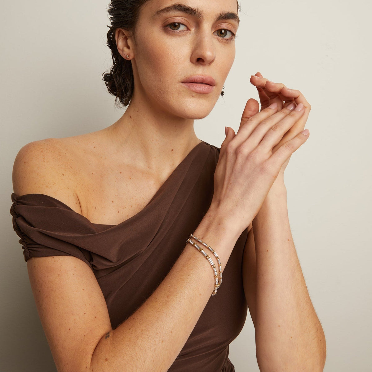 Model. Woman in a brown off-shoulder top sitting at a table with a neutral background