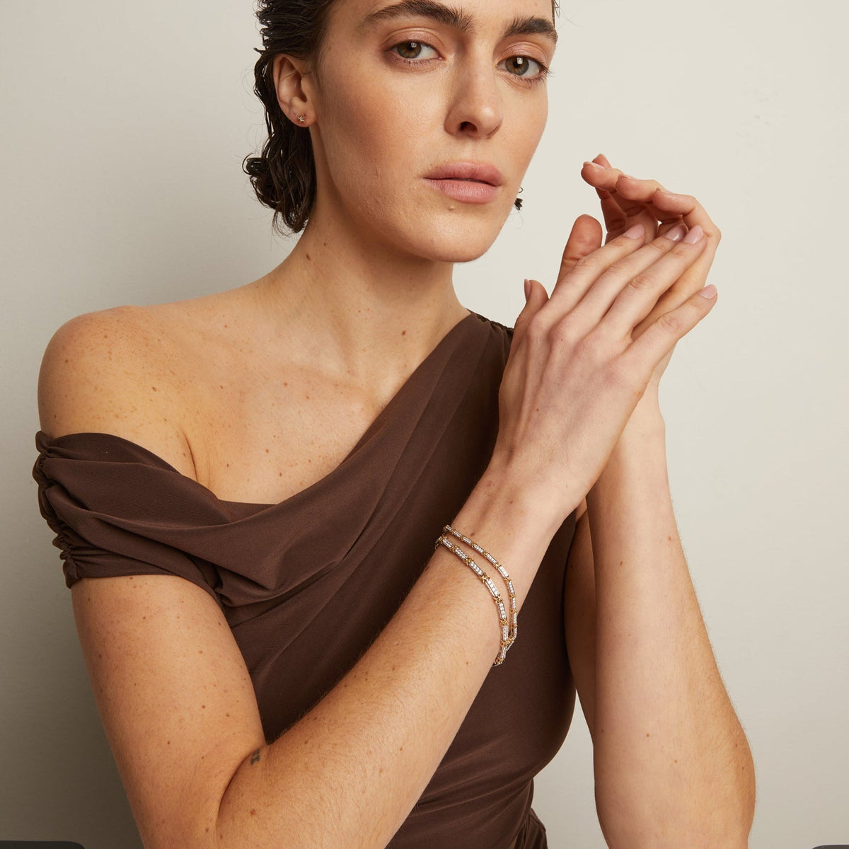 Model. Woman in a brown off-shoulder top sitting at a table with a neutral background