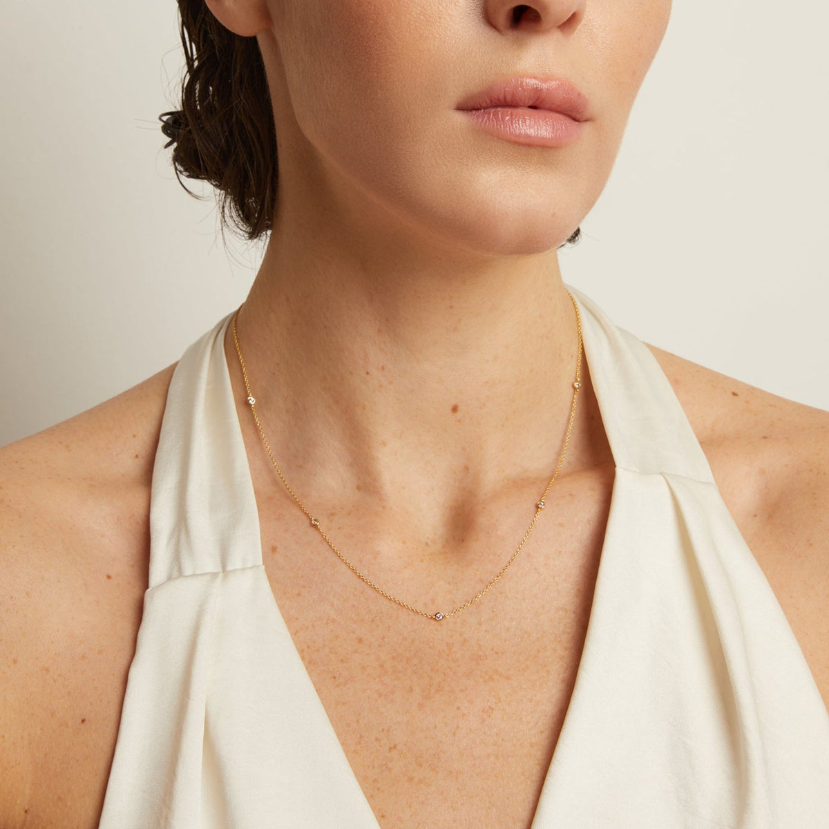 Model. Woman wearing a delicate gold necklace with a plain background