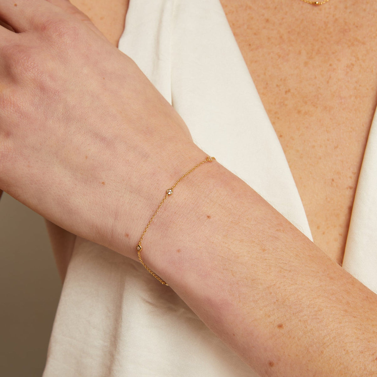 Model. Close-up of a person wearing a delicate gold bracelet and necklace against a neutral background