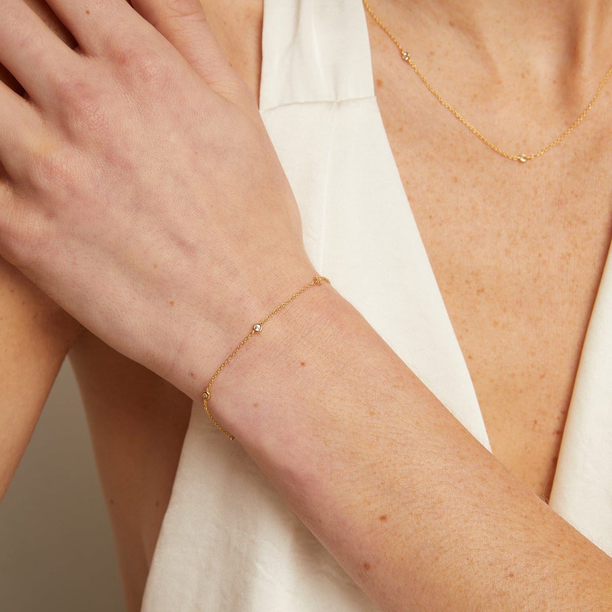 Model. Close-up of a person wearing a gold bracelet and necklace against a neutral background