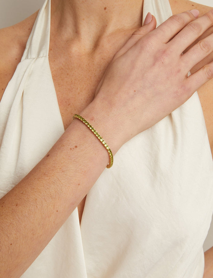 Person wearing a white sleeveless top with a gold bracelet on a neutral background