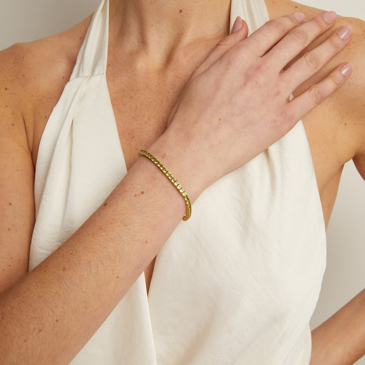 Person wearing a white sleeveless top with a gold bracelet on a neutral background
