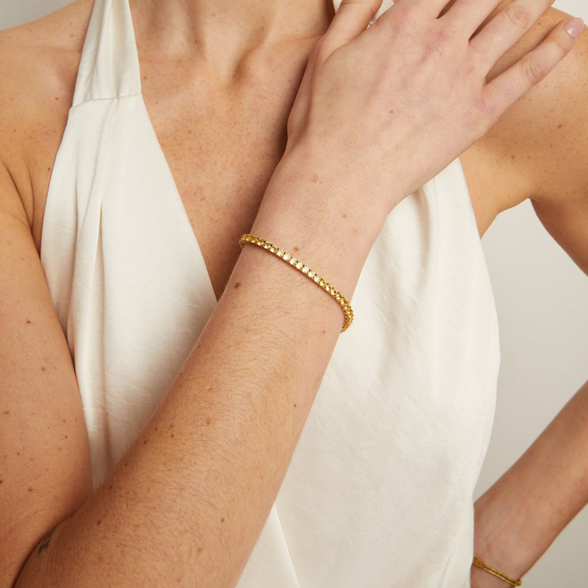 Model. Woman wearing a white halter neck top and gold bracelet on a plain background