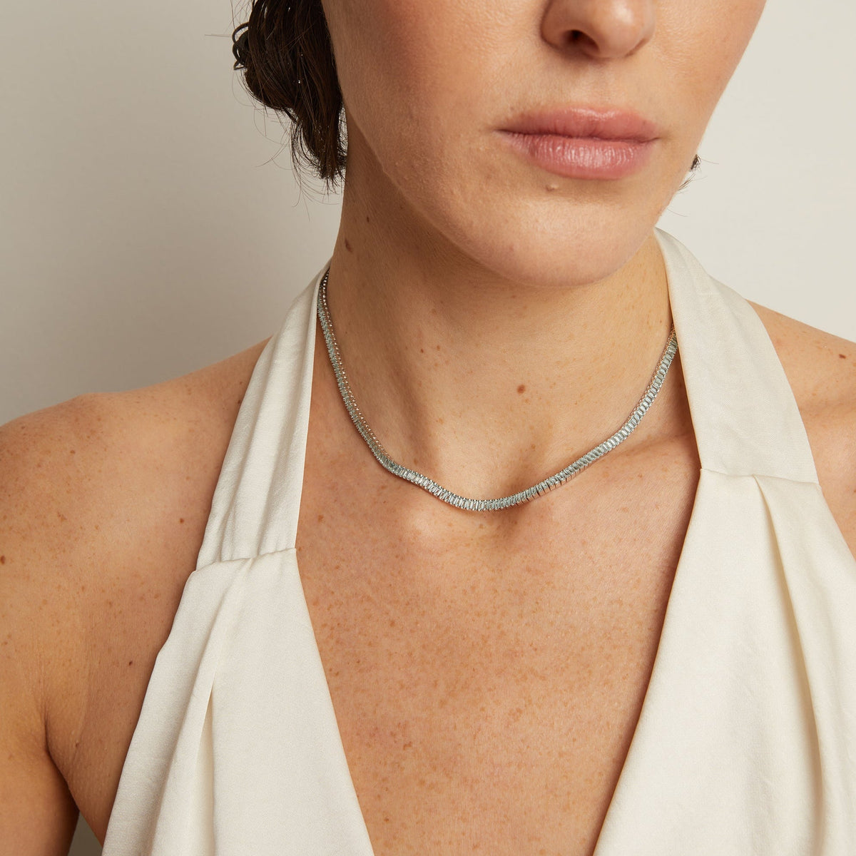 Model. Woman wearing a delicate silver necklace against a neutral background