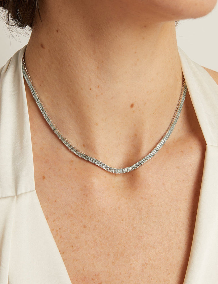 Necklace on a person wearing a white top against a neutral background