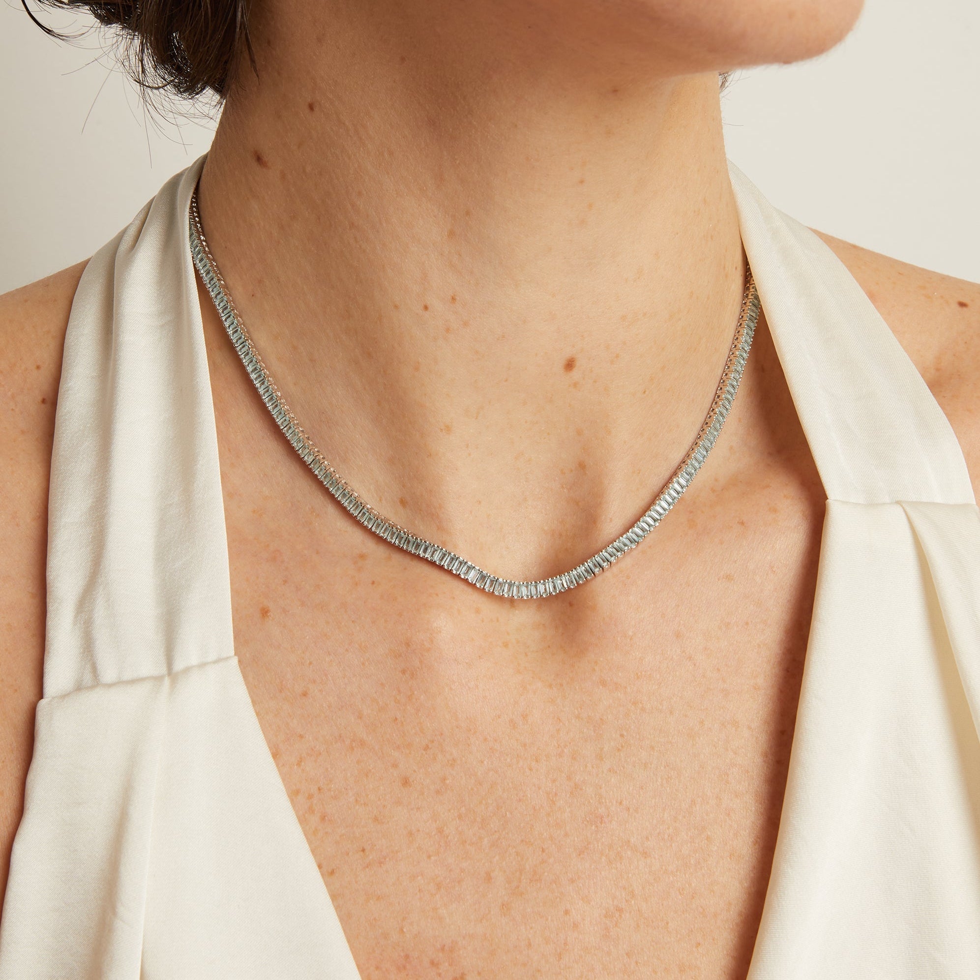 Necklace on a person wearing a white top against a neutral background