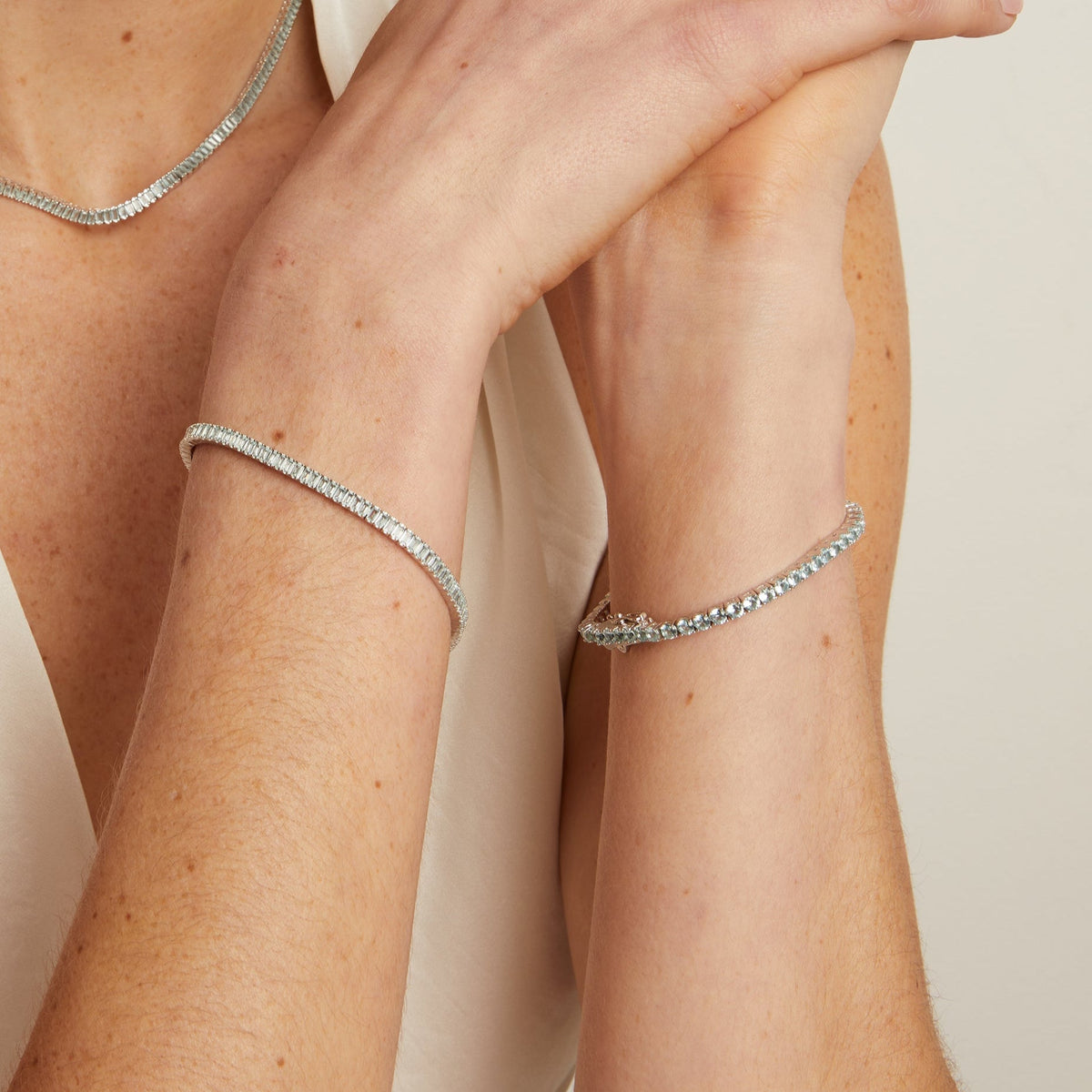 Model. Close-up of a person wearing a silver bracelet and necklace on a neutral background