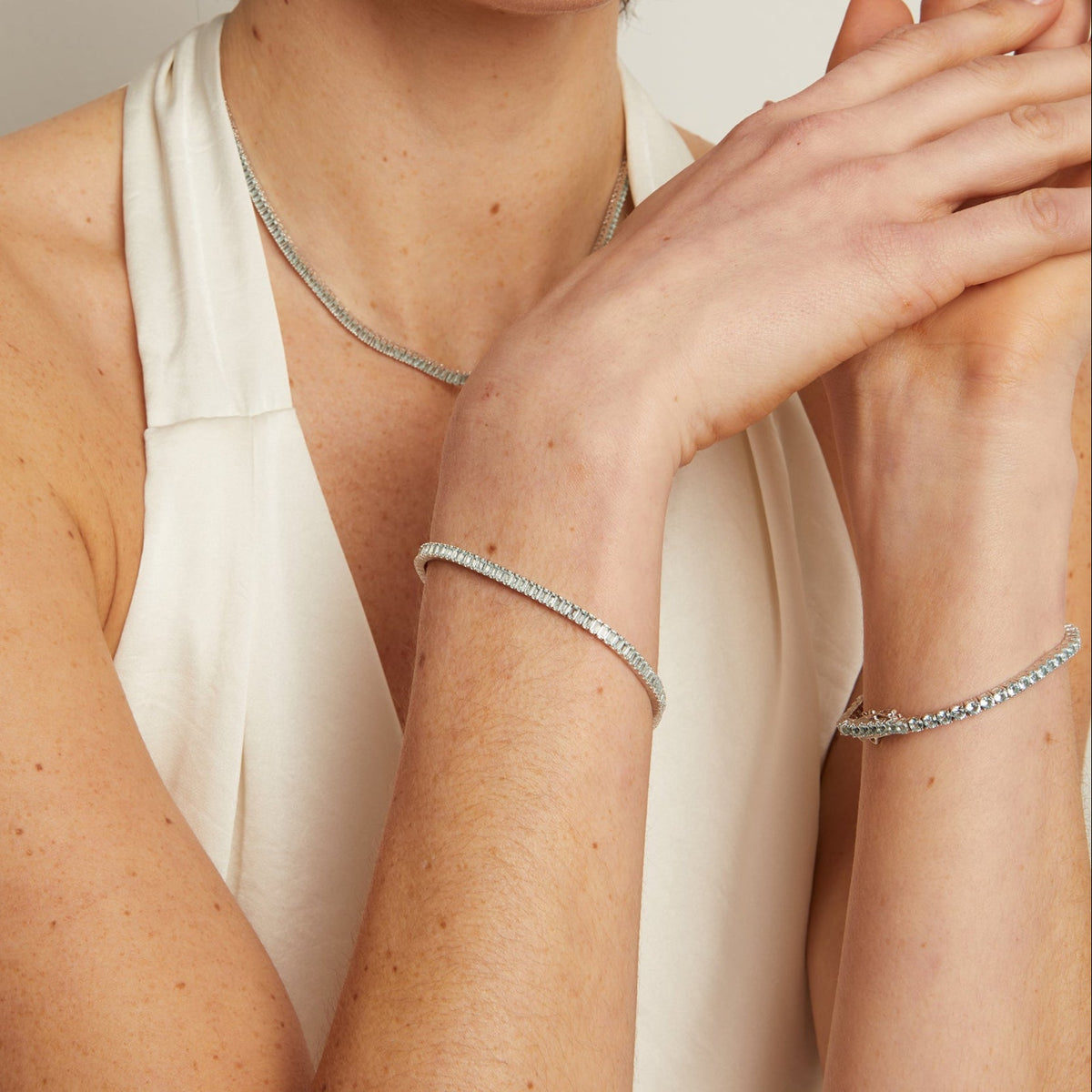 Model. Woman wearing a silver necklace and bracelet against a neutral background