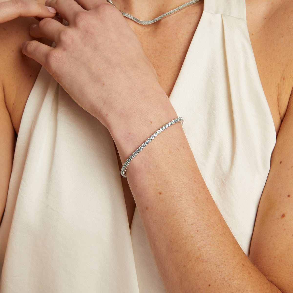 Model. Woman wearing a silver bracelet and necklace, with a plain background