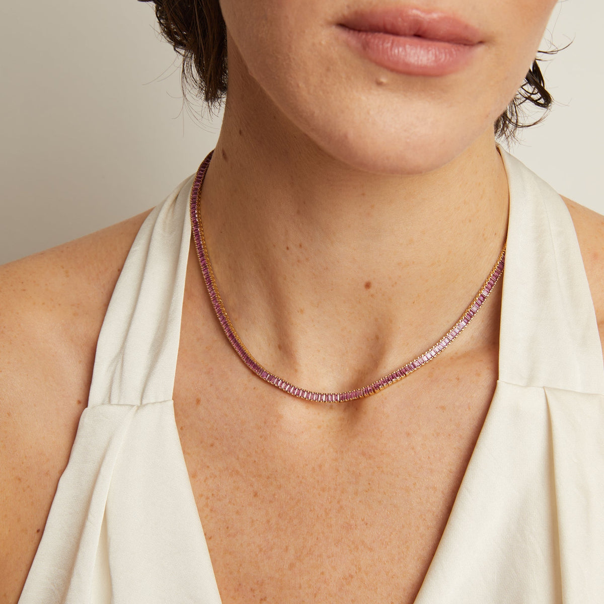 Model. Close-up of a woman wearing a delicate necklace with a plain background