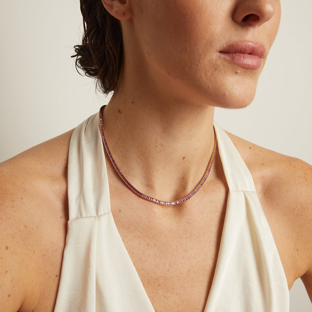 Model. Woman wearing a white halter neck top and a necklace against a neutral background