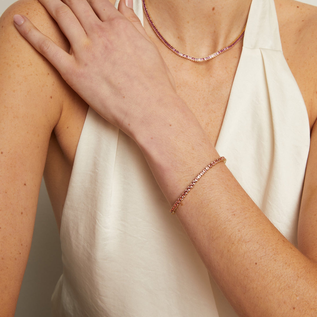 Model. Woman wearing a white top and rose gold jewelry on a neutral background