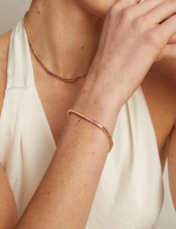 Close-up of a person wearing a delicate gold necklace and bracelet on a neutral background