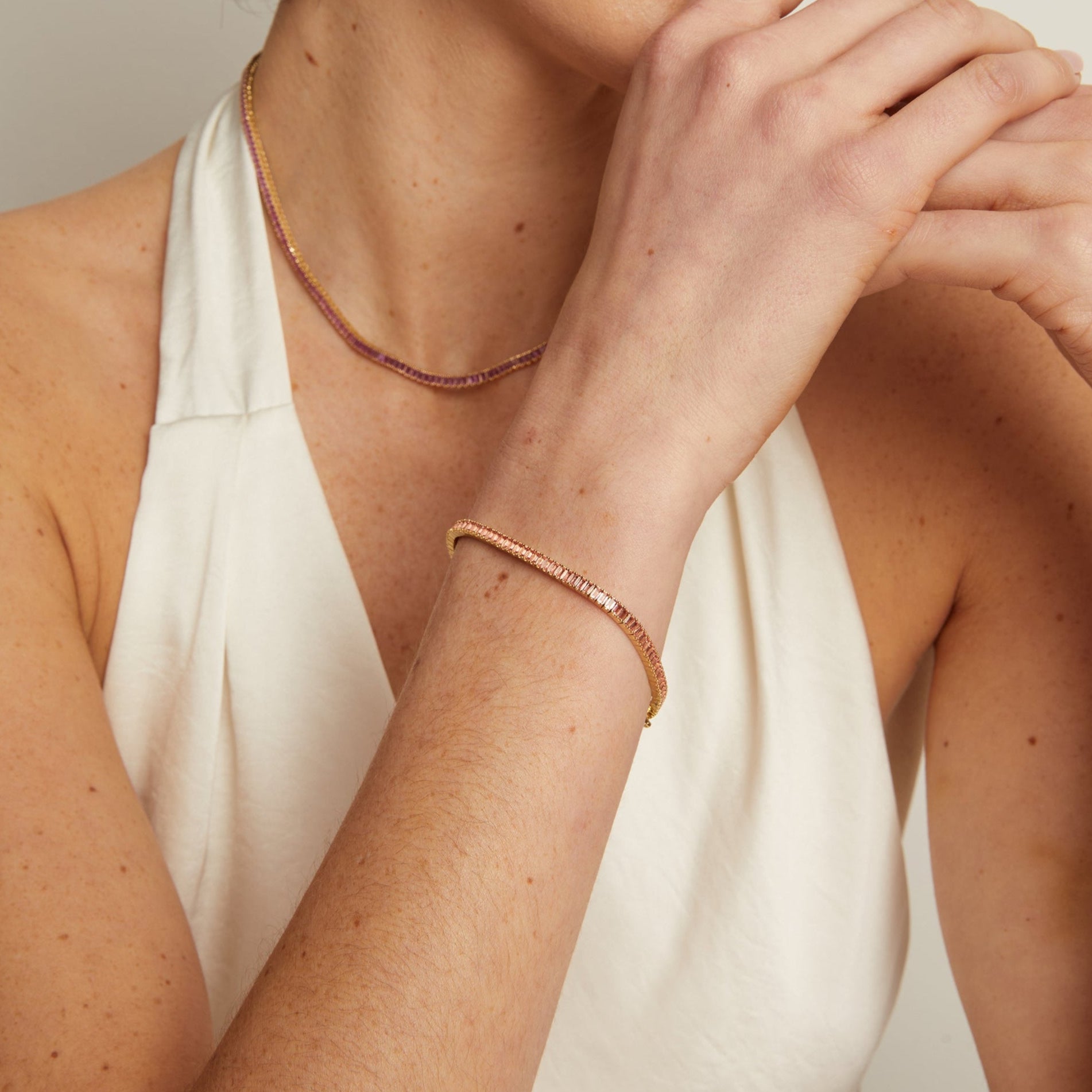 Close-up of a person wearing a delicate gold necklace and bracelet on a neutral background